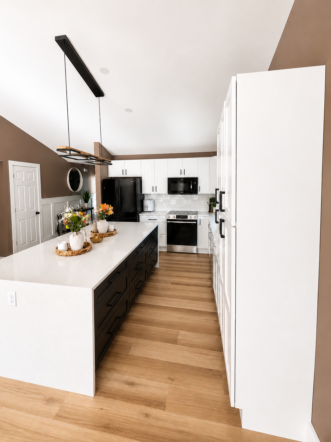 Remodeled kitchen with black island, white cabinetry and quartz waterfall counter